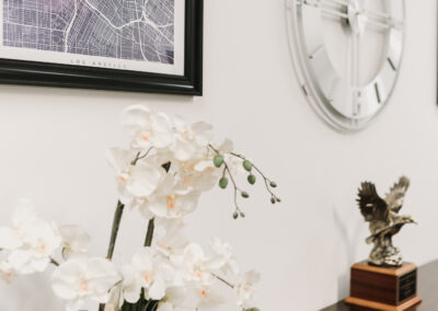 Office Image of slack legal with a white orchid, framed image, modern clock, credenza with a brass eagle award on top.